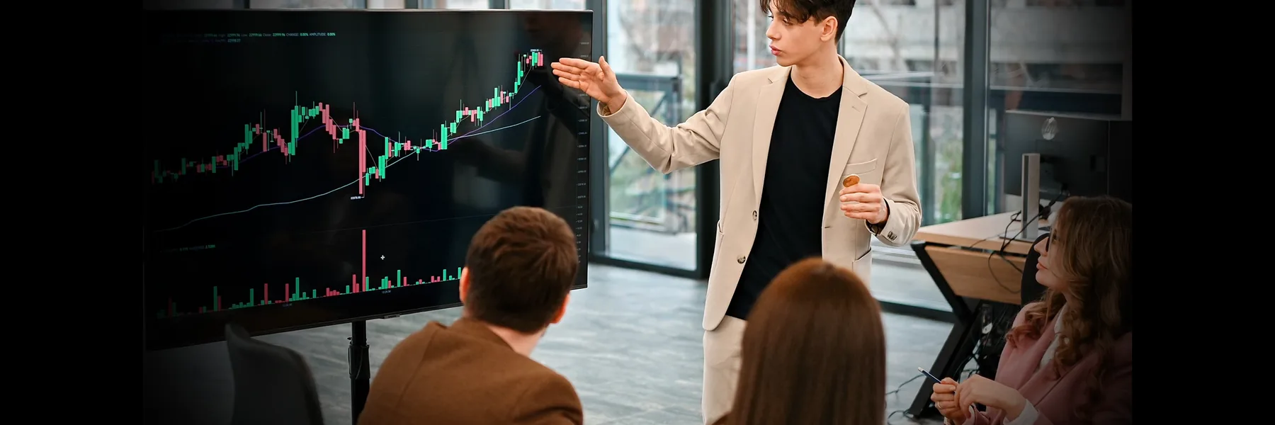 Presenter pointing at a candlestick chart on a large screen while a small group watches